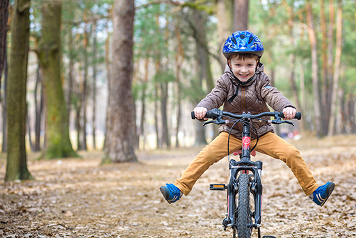 Young boy smiling whilst riding a bike in the woods