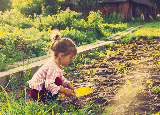 A young child crouching down outside with a spade