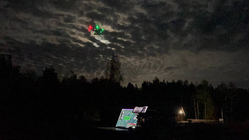Photograph of a drone in the air of a Scots Pine and mixed forest, Lithuania. There is a laptop on the ground showing the data from the drone.