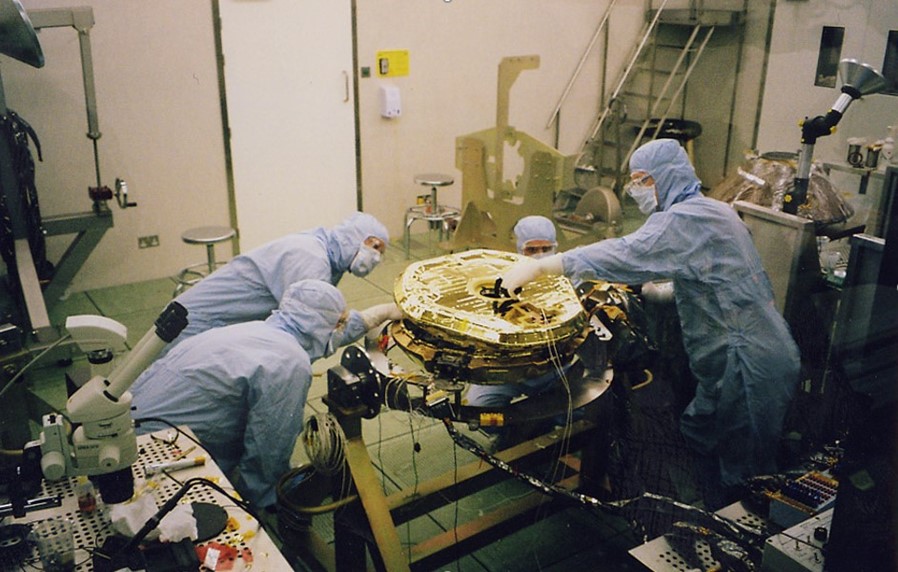 : A photograph of the Beagle 2 spacecraft with four engineers, within a cleanroom.
