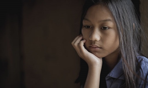 Close-up photograph of a young girl aged about 12. She is looking sad as she rests her chin on her hand.
