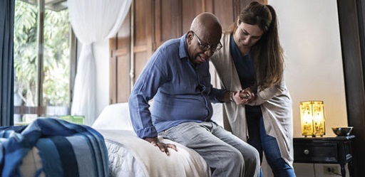 Photograph of a social care worker helping an older man to stand up.