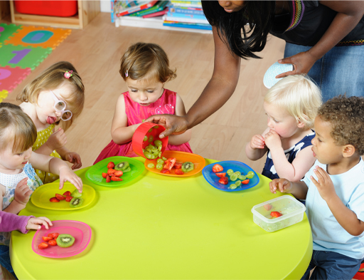 Photograph of children sat around a table eating fruit.