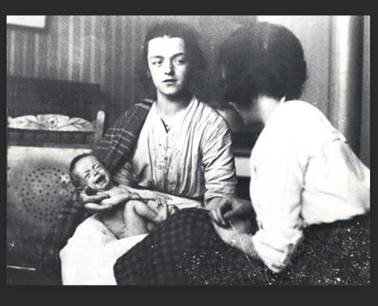 A black-and-white photograph of a woman holding a baby, in conversation with another woman.