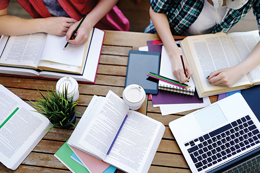 An image of a number of open books and a laptop on a table.
