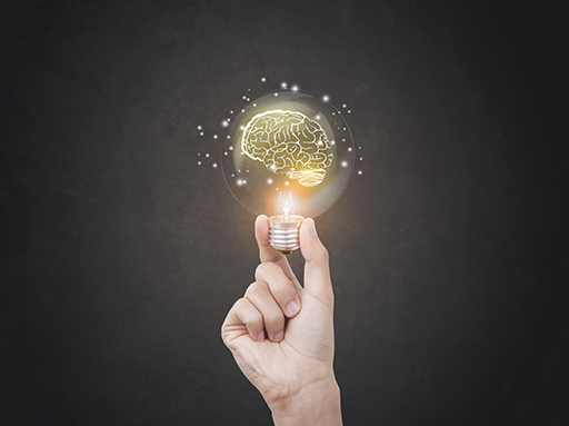 A hand holds an image of a lightbulb with an illuminated drawing of a brain inside it.