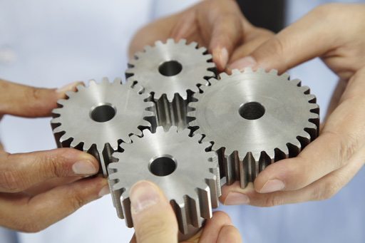 Four shiny, silver cogs, each held in someone’s hand and interlocking in the centre of the image.