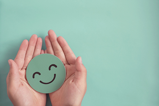 A pair of hands cupped together holding a smiling face drawn on a piece of card