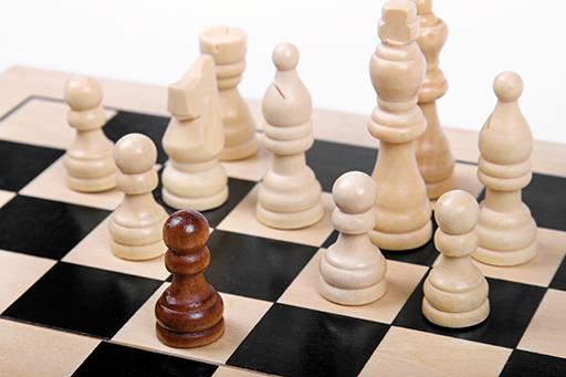 Chess pieces on a chess board, with one piece a different colour to the others.