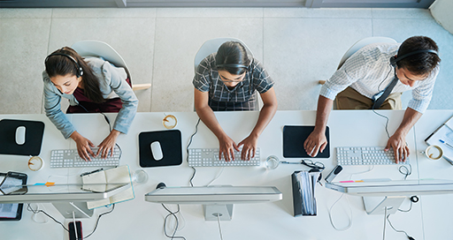 A birds-eye view of three people sitting at a desk working on a computer.