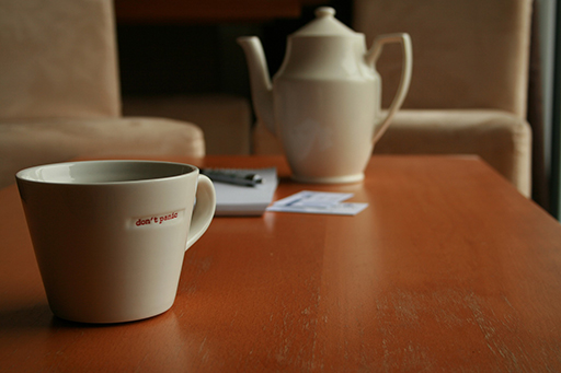 A tea pot and cup on a table. The cup says ‘don’t panic’ on it