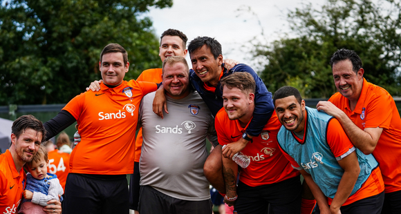 Group of men in Sands Utd football kits celebrating together.