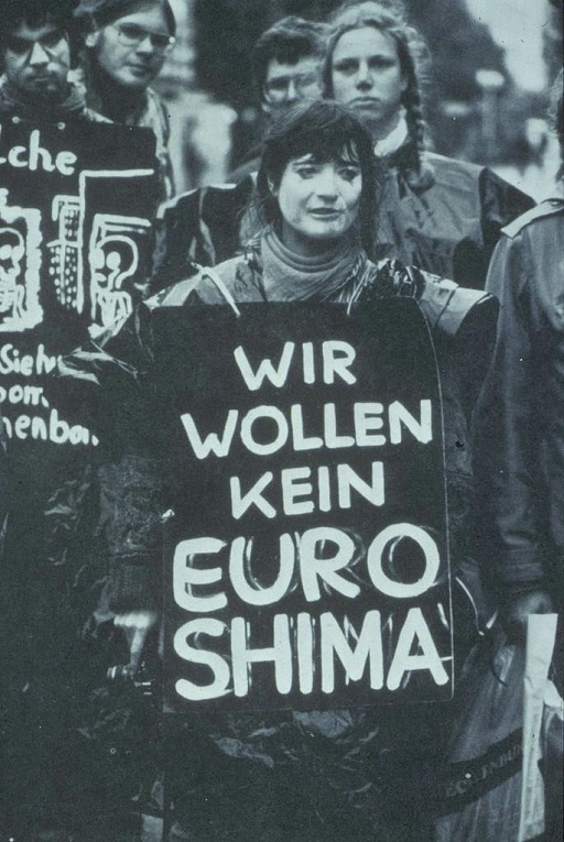 A black-and-white photograph of a woman holding a sign in a protest.
