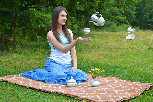 A person sitting on a picnic blanket, surrounded by levitating cups and saucers and a tea pot.