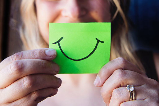 A person holding a post-it with a drawing of a smiley face