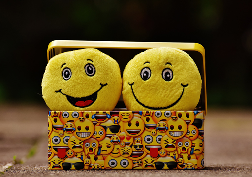 A box covered in emojis containing two smiling emoji cushions.