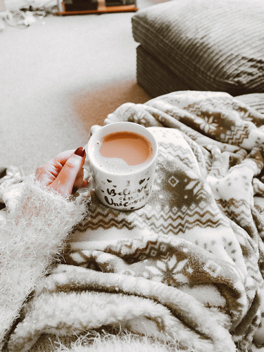 A person under a blanket holding a mug containing a hot drink.