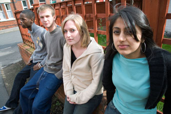 A photograph of a group of four teenagers, sitting on a wall at the side of a street.