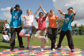 A photograph of dance teachers showing a group of children some street dance moves.