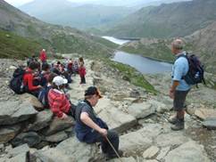 Photo of a group of hikers at the top of steep hill overlooking a river and mountains.