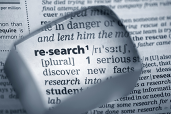 Photo of a magnifying glass over the dictionary term 'research'.