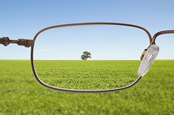 Photo of a view of a field and a tree in the distance seen through the left lens of pair of glasses.