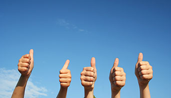 Photo of five hands gesturing a thumbs-up, against a blue sky.