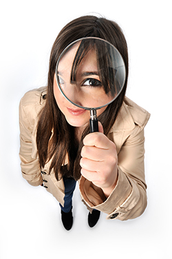 Photo of a woman holding a magnifying glass to her eye.