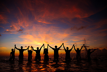 Photo of several people stood in the sea holding hands at sunset.