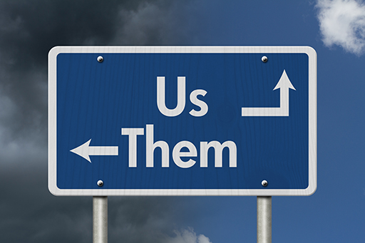 An image of a road sign saying ‘Us’ on the top line and ‘Them’ on the line below.