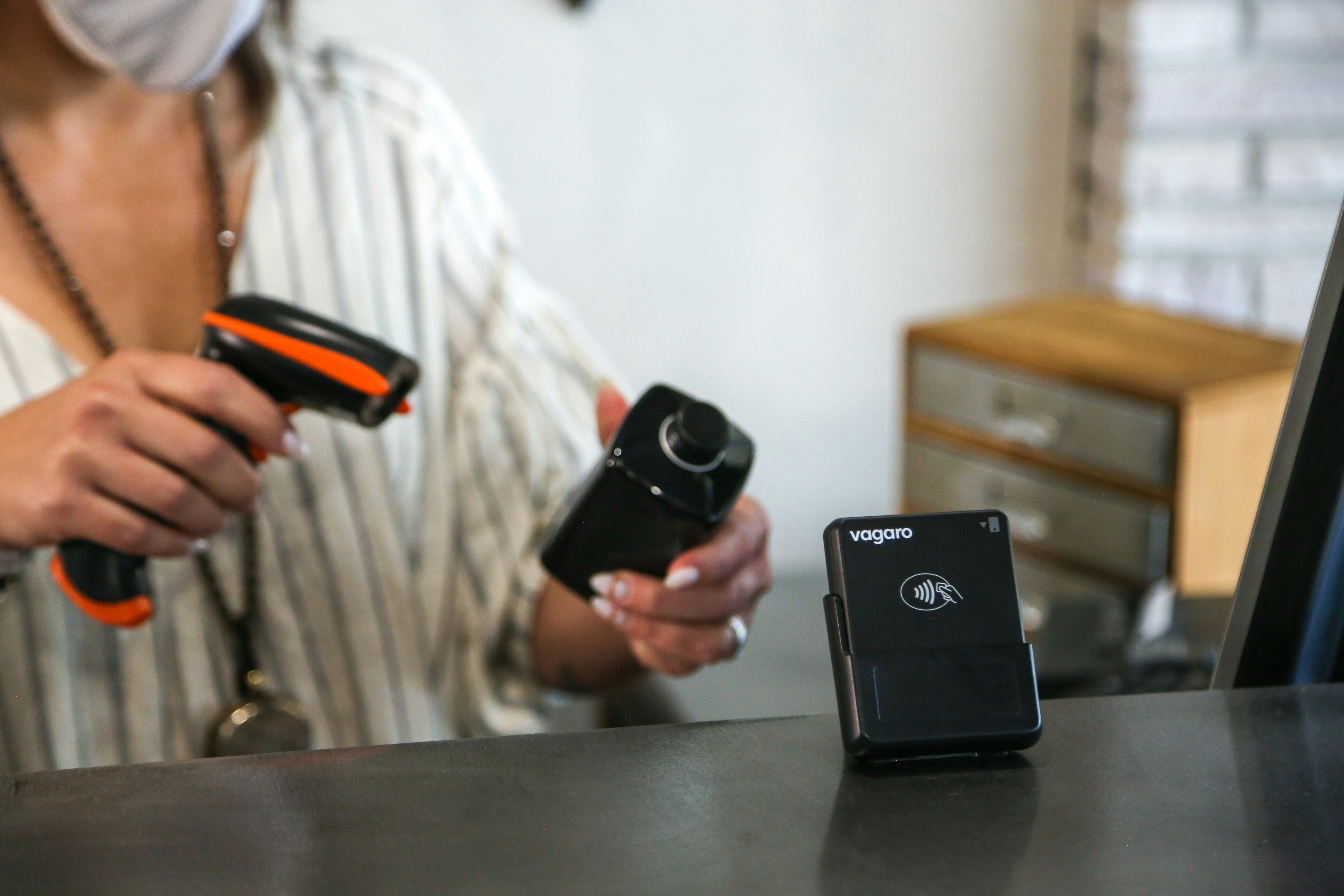 A woman at a front desk is scanning a hair styling product with a barcode scanner. The front desk has a credit card reader on