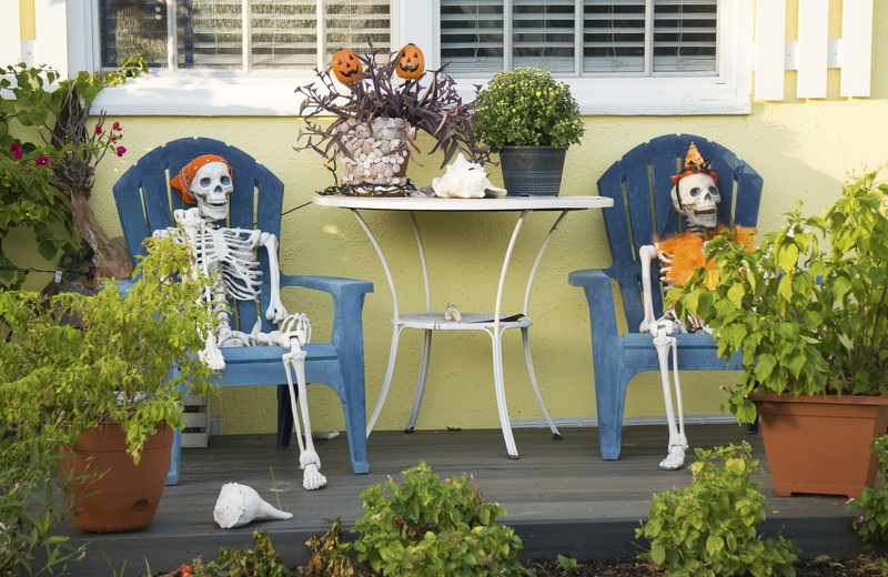 Halloween skeletons sitting in beach chairs on a porch outside a house.