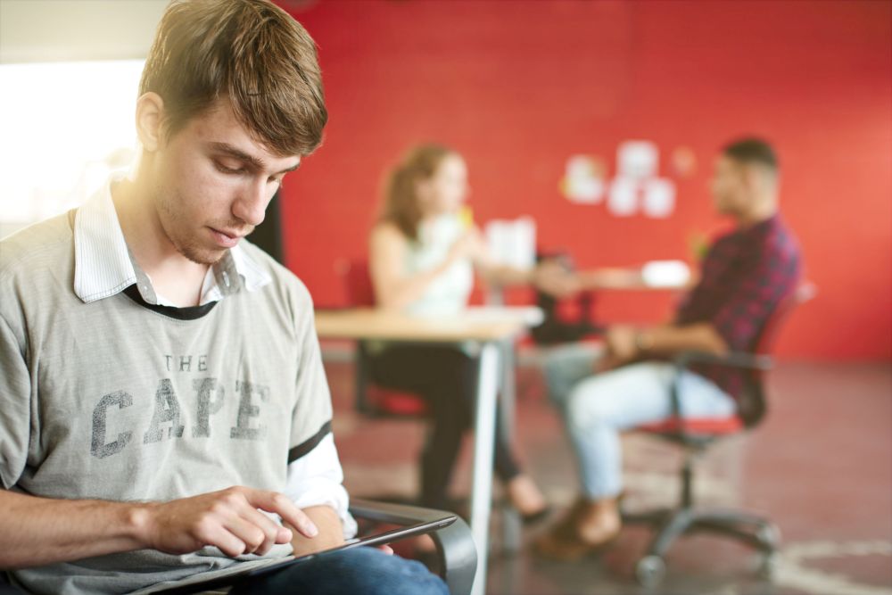 Student using a tablet while two ther students are talking in the background - emphasising varied participation