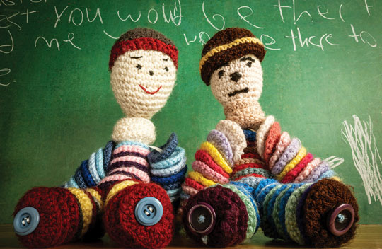 A colour image of two knitted dolls seated on a table side by side.