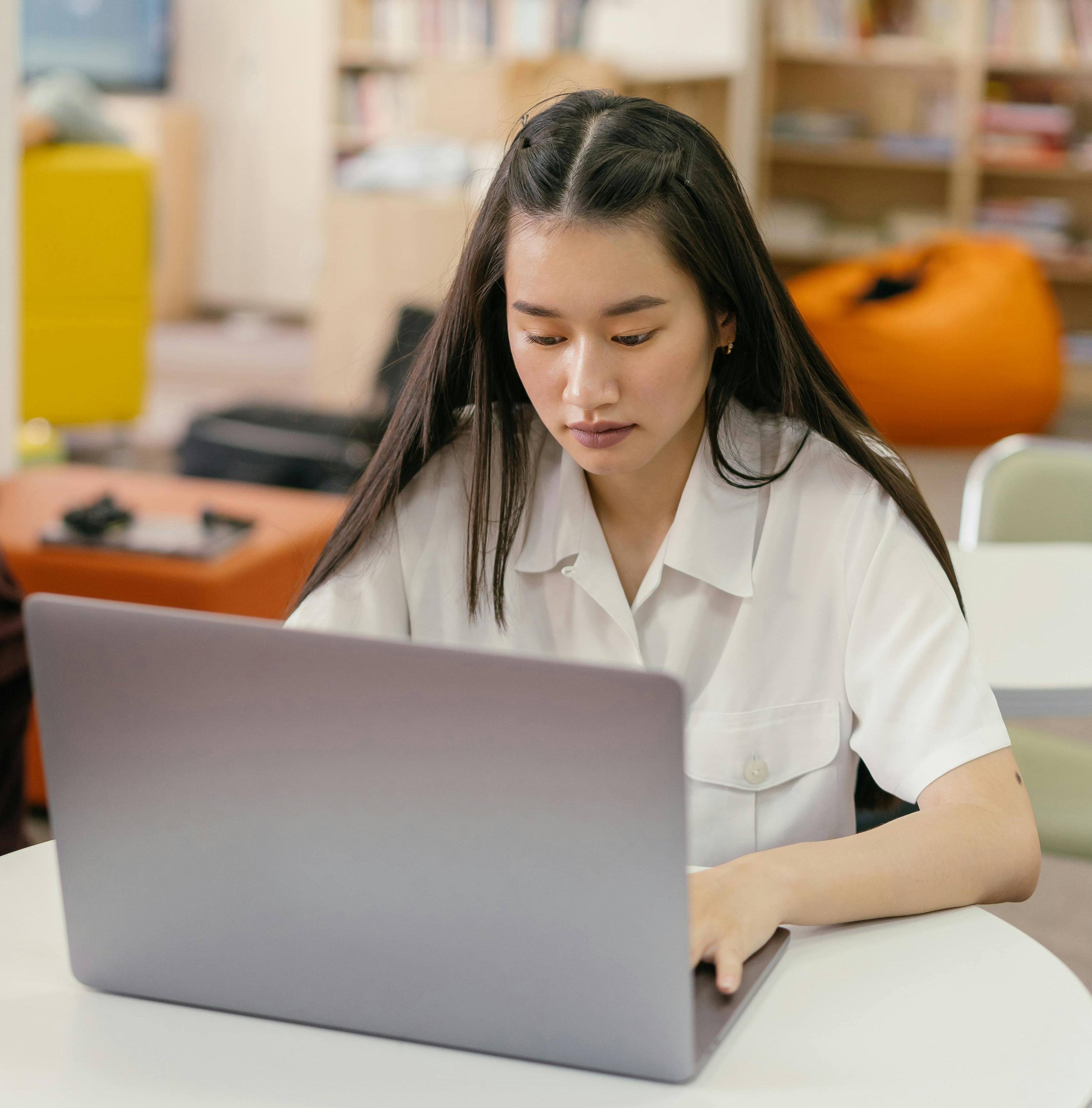 Woman sat at a table typing on a laptop.