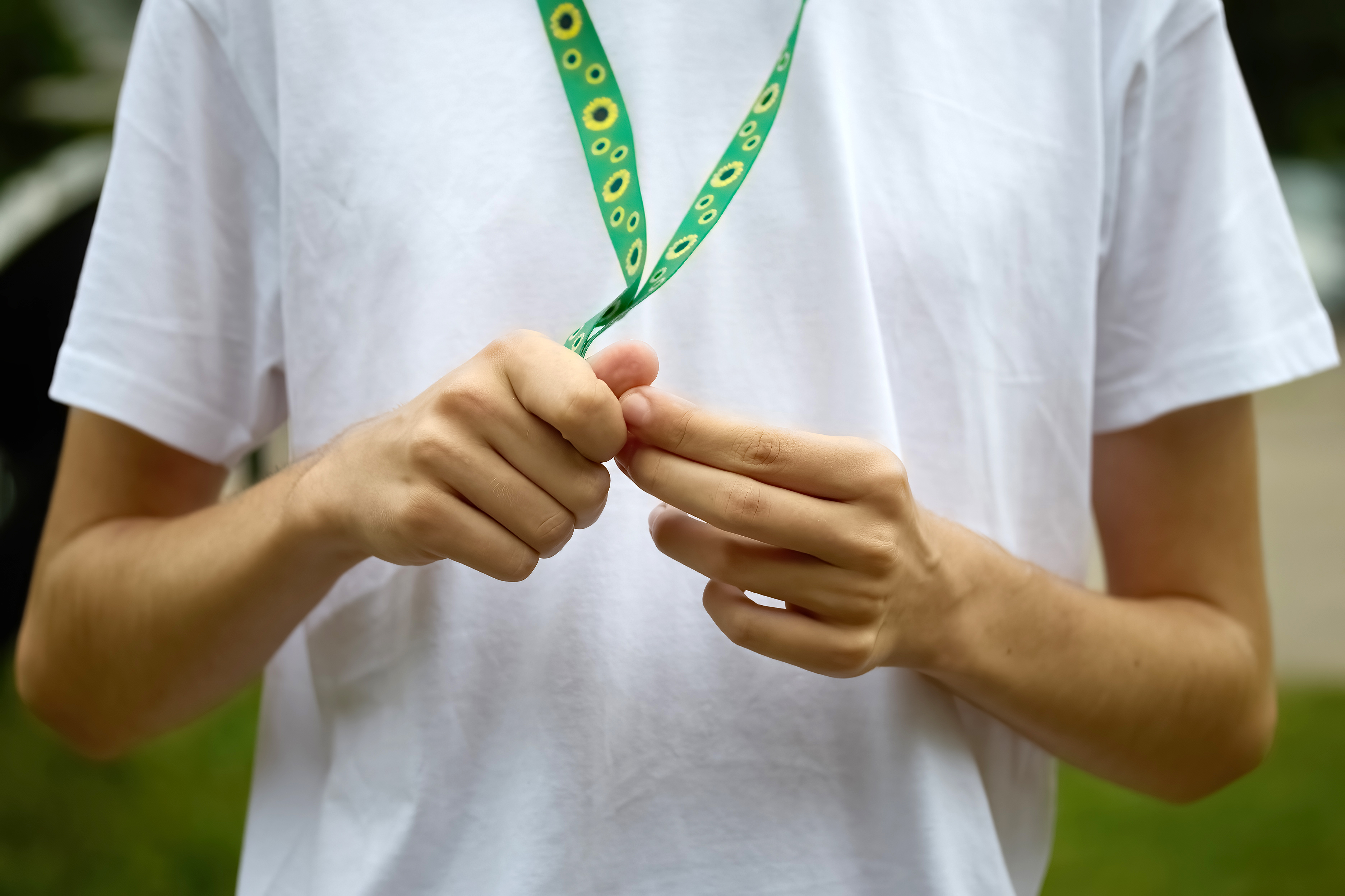 A person wearing a white shirt fiddles with a green lanyard adorned with sunflower designs