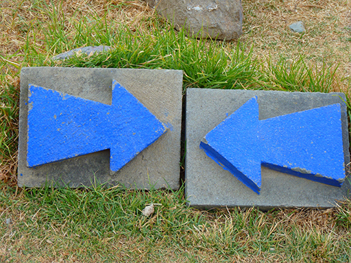 Two blue arrows painted on paving slabs pointing twoards each other.