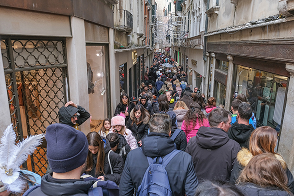 Photograph showing a very crowded small street with high rise buildings in Venice at carnival time.