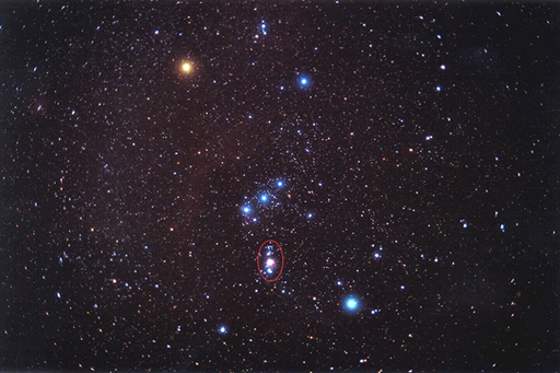 A photograph of the night sky with Orion circled.