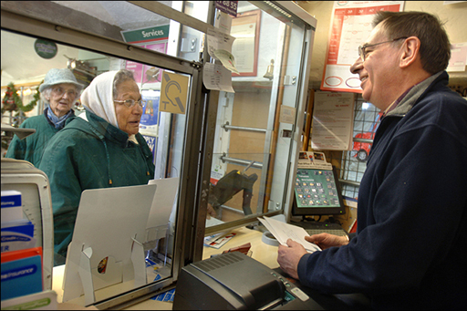 This photograph shows a pensioner picking up her pension at the post office.
