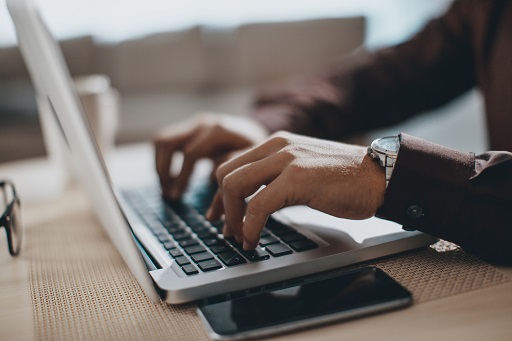 A photograph of a person’s hands typing on a laptop.