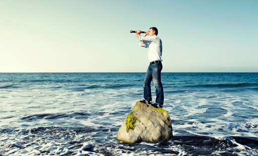 Man standing on a rock looking through a telescope.