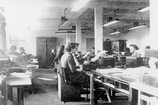 A black-and-white photograph of a number of women in an office at machines.