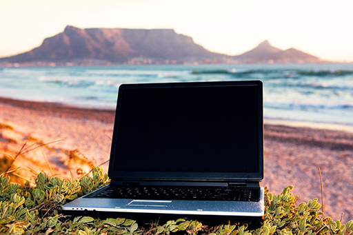 A photograph is of an open laptop, but a beach and the sea in the background.