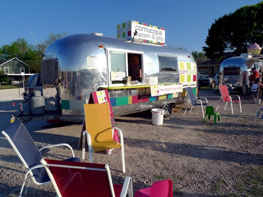 An image of a silver caravan-style mobile shop and café, with chairs for customers in front of it.