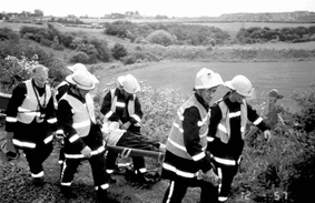 Image showing an emergency rescue team carrying a stretcher beside a railway track in an exercise involving 4 people to carry the stretcher and 2 to look after the casualty