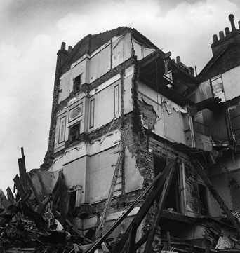 Photograph shows the damage to 52 Tavistock Square, destroyed by bombs in 1941. One side of the house is still standing, but several other sides have collapsed, and there are piles of rubbles surrounding the site.