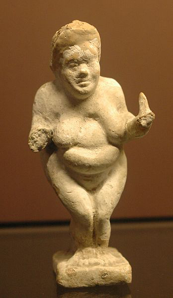 Terracotta figurine of a standing woman with large breasts, belly and hips.