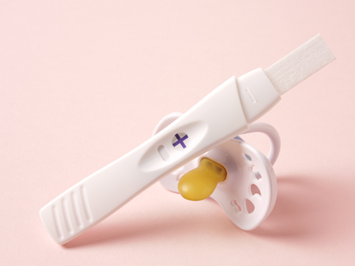 Pregnancy test kit showing a positive result and a baby’s dummy.