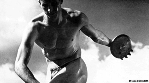 Still image from the film Olympia, of a male athlete posed as though about to throw the discus he is holding in his left hand.